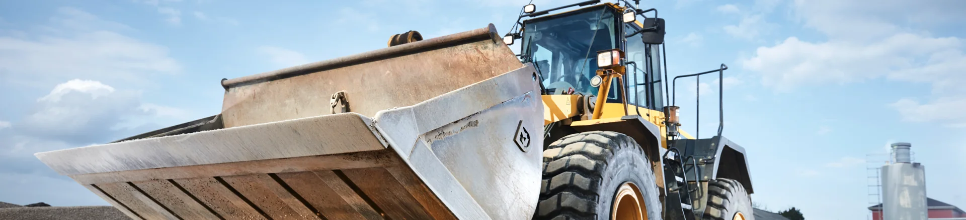 A yellow front-end loader with a large bucket attachment is parked outdoors on a construction site under a partly cloudy sky.