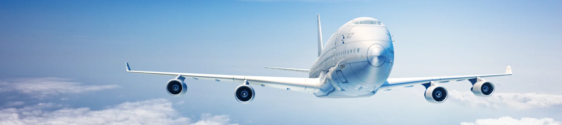 A large commercial airplane flies above the clouds in a clear blue sky, viewed from the front left side.