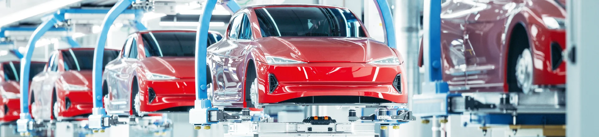 Multiple red cars are assembled and suspended on robotic platforms inside a modern automotive manufacturing facility.