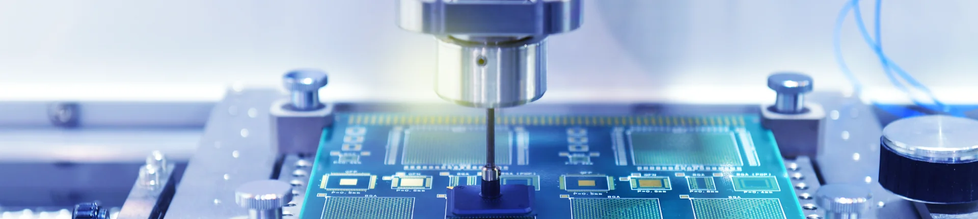 A close-up view of a machine tool precisely working on a green printed circuit board in an electronics manufacturing setting.